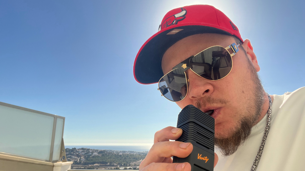 Zufriedener Mann sitzt entspannt draußen bei Sonnenschein und hält einen frisch gereinigten, glänzenden Vaporizer in der Hand.