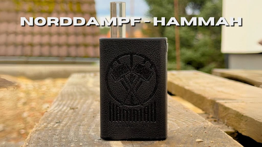 Der Norddampf Hammah Vaporizer steht auf einem Holztisch im Freien, mit deutlich sichtbarem Logo auf der Vorderseite und dem Schriftzug „Norddampf-Hammah“ darüber.