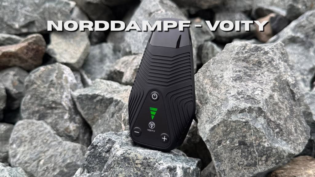 Der Norddampf Voity Vaporizer steht auf einem Haufen grauer Steine, mit seinem markanten schwarzen Gehäuse, grünem LED-Display und der Aufschrift „Norddampf - Voity“ darüber.